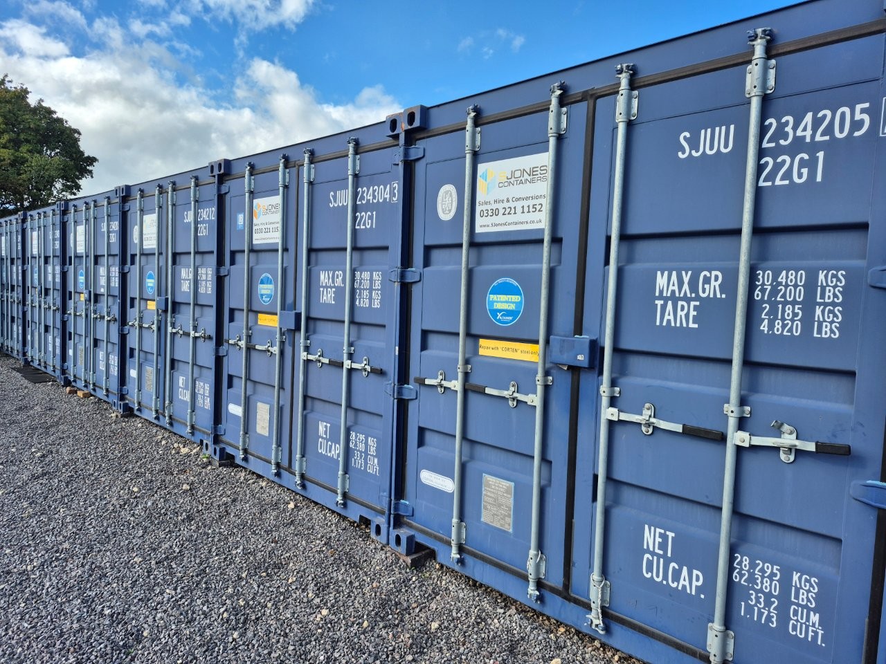 Row of secure blue self-storage shipping containers on a gravel lot at The Hawthorns Estate in Staunton, Gloucestershire.